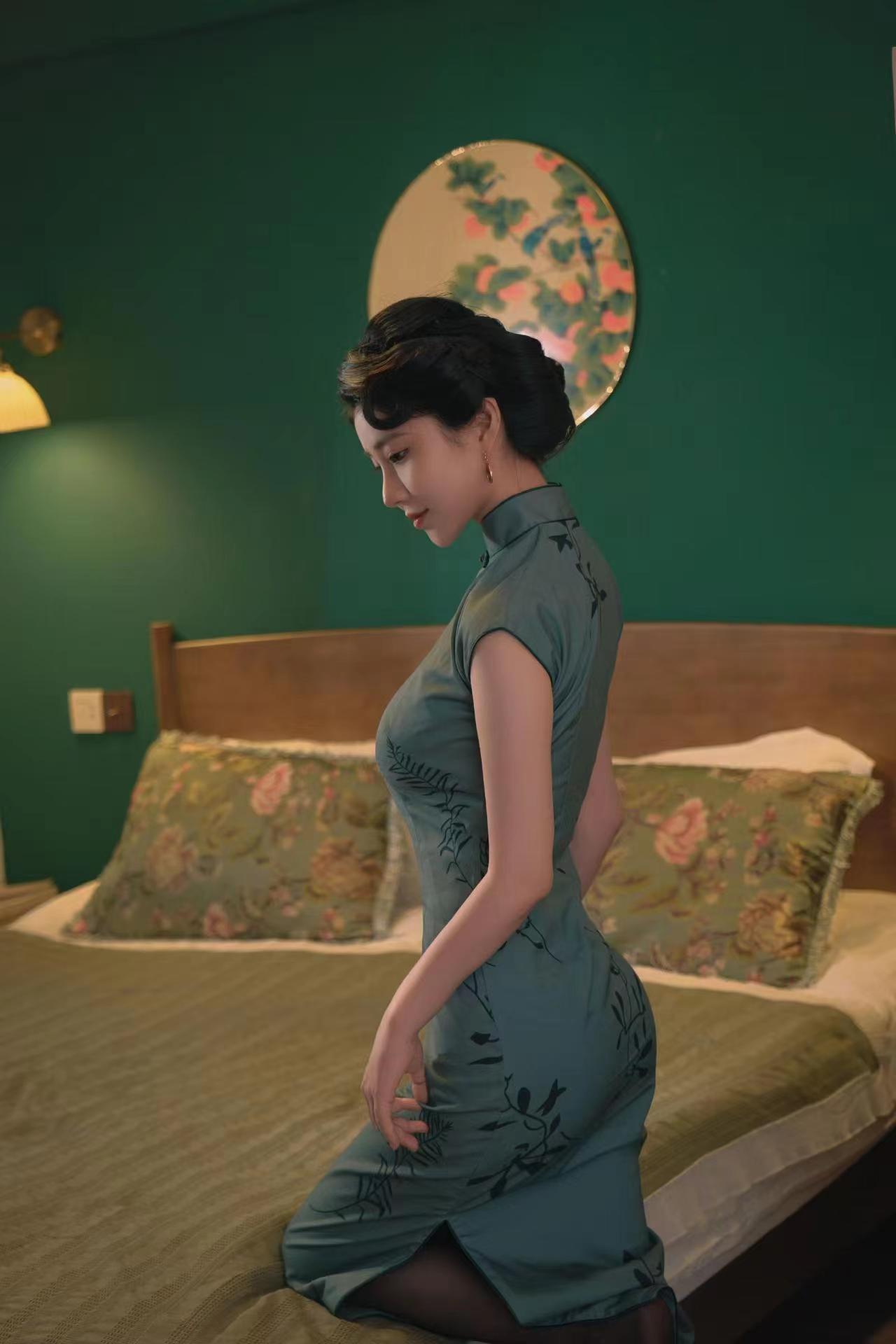 The slit of the emerald cheongsam revealed a section of her jade-like legs, which were faintly visible between the dark red silk quilt.
